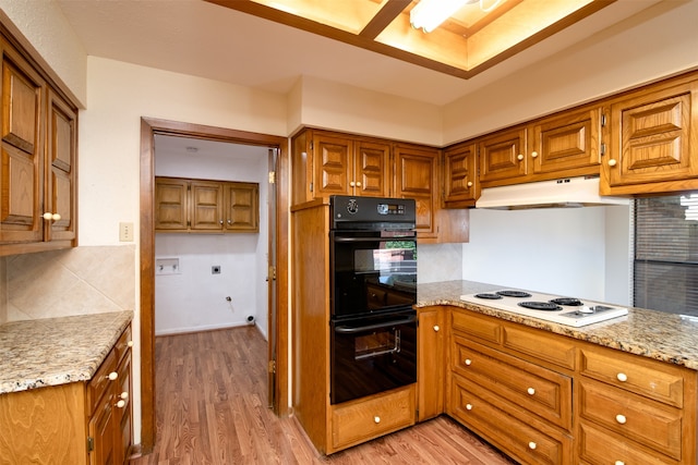 kitchen featuring white electric cooktop, backsplash, light hardwood / wood-style flooring, double oven, and light stone counters