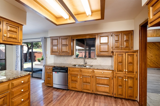 kitchen featuring tasteful backsplash, light stone counters, stainless steel dishwasher, light hardwood / wood-style floors, and sink