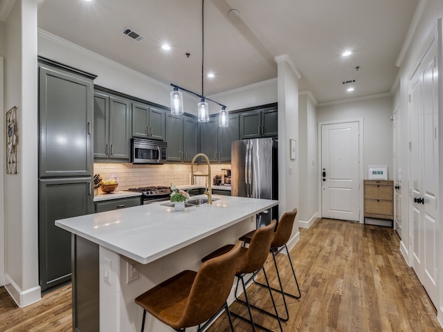 kitchen featuring an island with sink, light hardwood / wood-style flooring, sink, pendant lighting, and stainless steel appliances