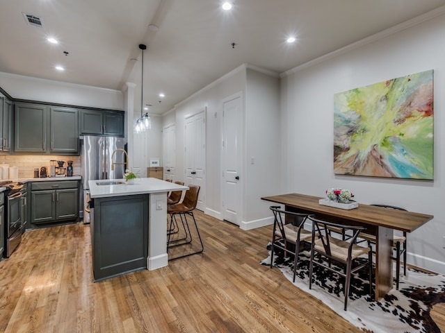 kitchen with a kitchen island with sink, hanging light fixtures, backsplash, crown molding, and light wood-type flooring