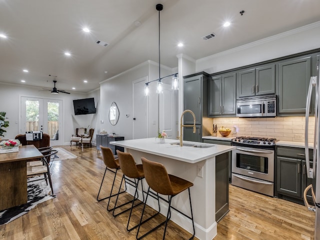 kitchen with appliances with stainless steel finishes, sink, a center island with sink, and pendant lighting