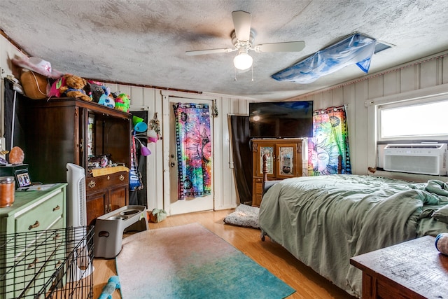 bedroom with wood walls, a textured ceiling, cooling unit, ceiling fan, and light hardwood / wood-style flooring