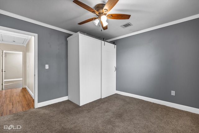 unfurnished bedroom featuring ceiling fan, dark colored carpet, ornamental molding, and a barn door