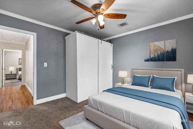 bedroom featuring ceiling fan, ornamental molding, a barn door, and hardwood / wood-style floors