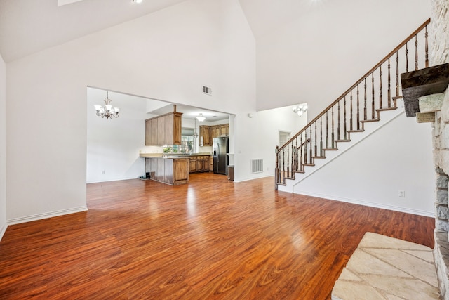 unfurnished living room featuring wood-type flooring, high vaulted ceiling, and an inviting chandelier