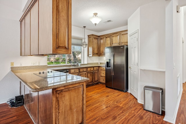 kitchen with sink, stainless steel refrigerator with ice dispenser, kitchen peninsula, pendant lighting, and black electric stovetop