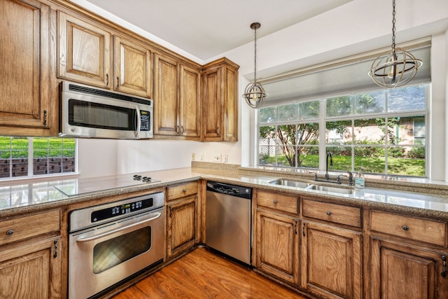 kitchen with stainless steel appliances, a sink, a notable chandelier, brown cabinetry, and decorative light fixtures