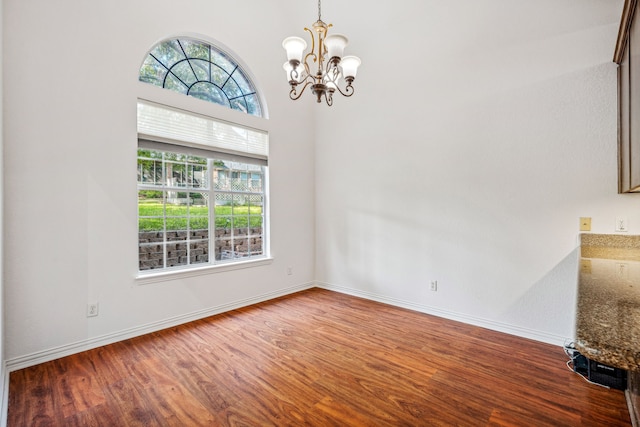unfurnished dining area featuring baseboards, wood finished floors, and a notable chandelier