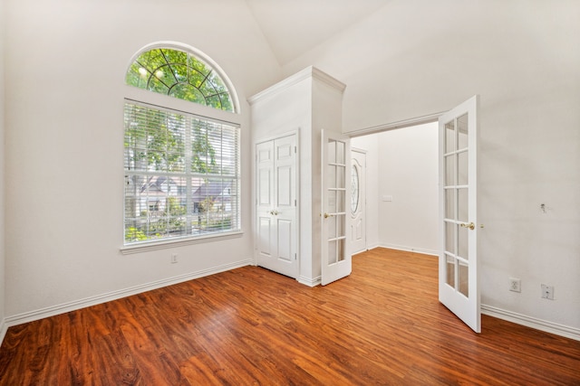 unfurnished bedroom featuring high vaulted ceiling, wood finished floors, a closet, french doors, and baseboards