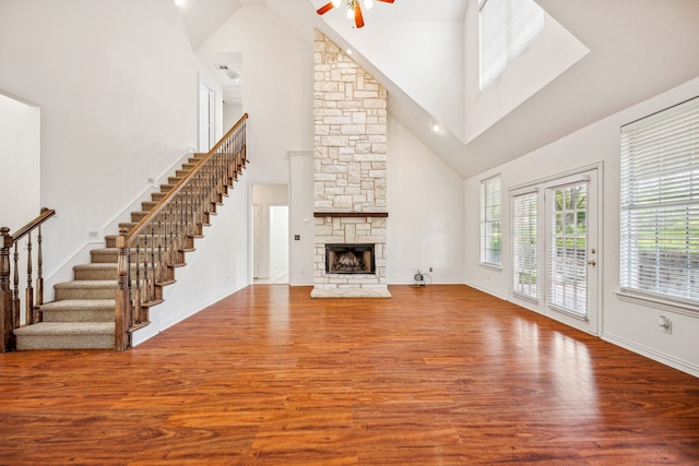 unfurnished living room featuring ceiling fan, a stone fireplace, wood-type flooring, and a towering ceiling