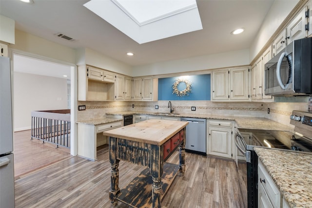 kitchen with backsplash, appliances with stainless steel finishes, sink, and light hardwood / wood-style flooring