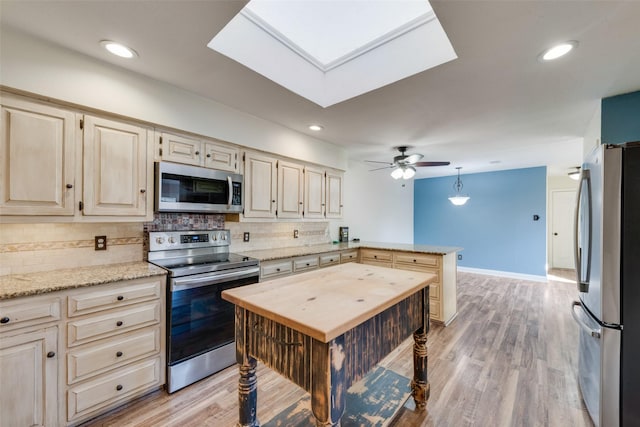 kitchen with light hardwood / wood-style floors, appliances with stainless steel finishes, tasteful backsplash, light stone countertops, and a center island