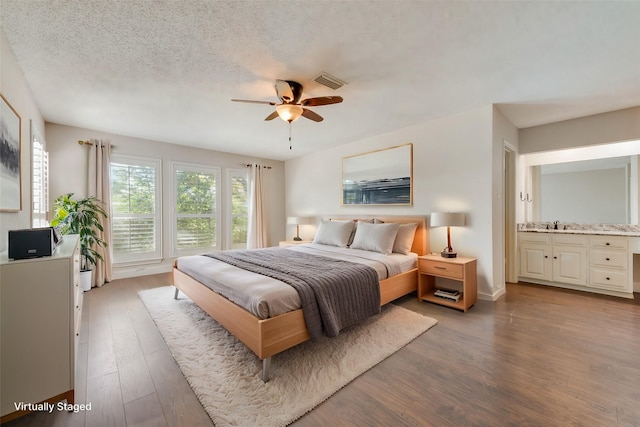 bedroom with ceiling fan, a textured ceiling, light hardwood / wood-style flooring, and connected bathroom