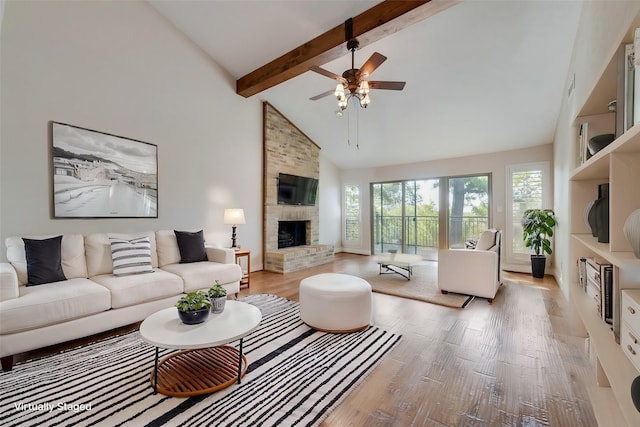 living room with a stone fireplace, ceiling fan, light wood-type flooring, high vaulted ceiling, and beam ceiling