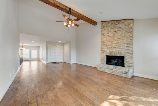 unfurnished living room featuring ceiling fan with notable chandelier, light hardwood / wood-style floors, a fireplace, and vaulted ceiling with beams