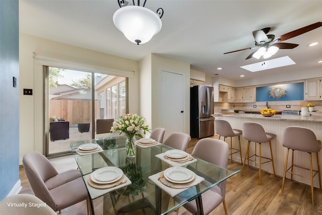 dining area with ceiling fan, a skylight, and light hardwood / wood-style flooring