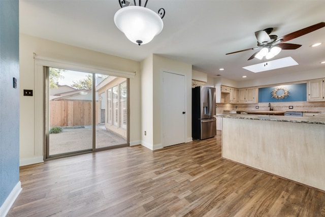 kitchen featuring stainless steel fridge with ice dispenser, a skylight, tasteful backsplash, light brown cabinetry, and light hardwood / wood-style flooring