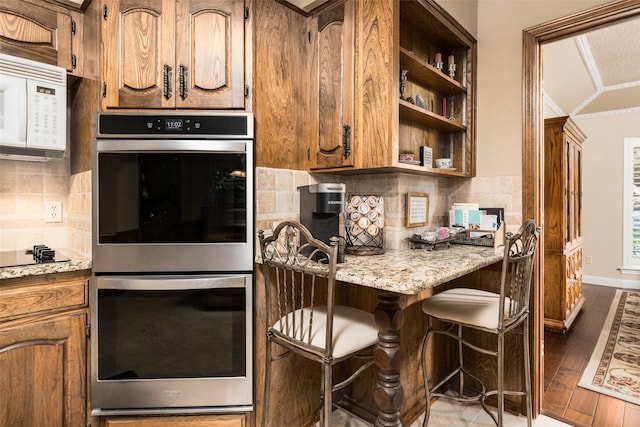 kitchen with backsplash, black electric stovetop, dark hardwood / wood-style floors, double oven, and light stone counters