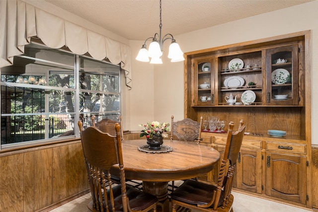 tiled dining area with wooden walls, a chandelier, and a textured ceiling