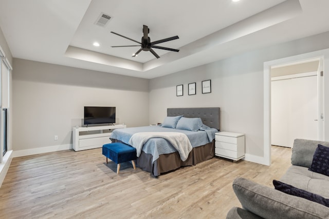 bedroom with ceiling fan, a tray ceiling, and light hardwood / wood-style flooring