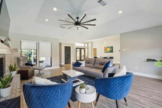 living room featuring a fireplace, light wood-type flooring, a raised ceiling, and ceiling fan