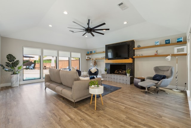 living room featuring a fireplace, ceiling fan, a tray ceiling, and light hardwood / wood-style flooring