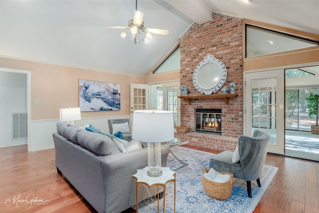 living room featuring vaulted ceiling with beams, a fireplace, light hardwood / wood-style floors, and ceiling fan