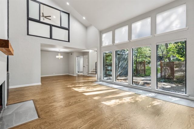 unfurnished living room featuring high vaulted ceiling, hardwood / wood-style flooring, and ceiling fan with notable chandelier