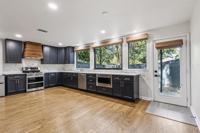 kitchen featuring custom exhaust hood, light countertops, visible vents, light wood-style flooring, and appliances with stainless steel finishes