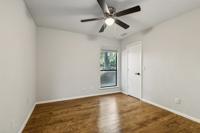 empty room featuring a ceiling fan, visible vents, baseboards, and wood finished floors