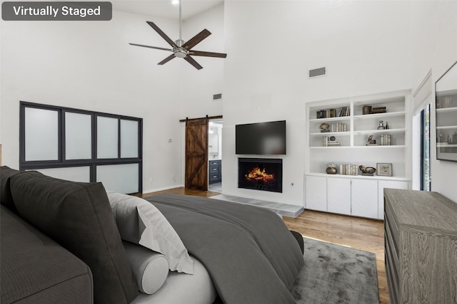 living area with visible vents, a high ceiling, a barn door, a ceiling fan, and wood finished floors