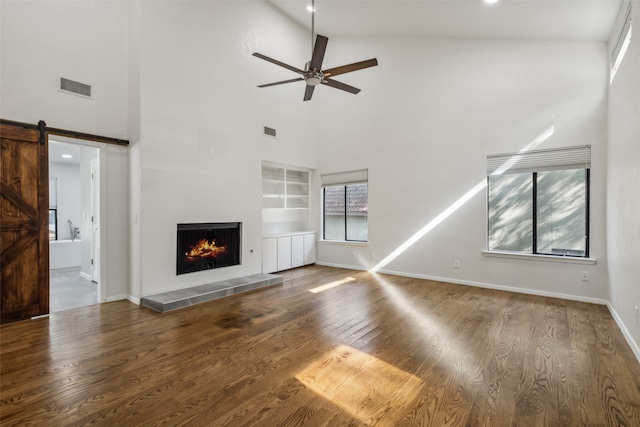 unfurnished living room with a barn door, built in features, hardwood / wood-style floors, ceiling fan, and high vaulted ceiling