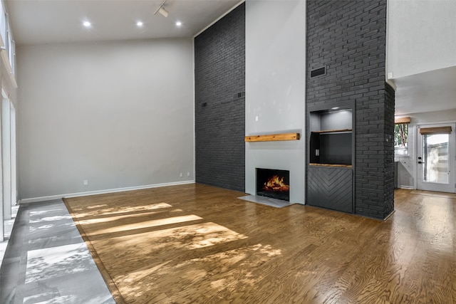 unfurnished living room featuring rail lighting, a towering ceiling, wood finished floors, a warm lit fireplace, and baseboards