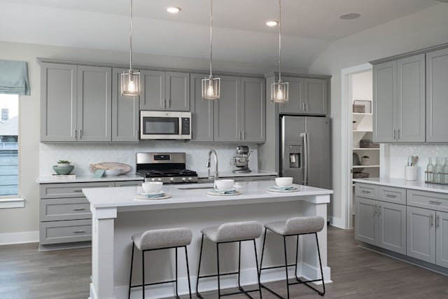 kitchen with vaulted ceiling, appliances with stainless steel finishes, gray cabinetry, and a kitchen island with sink