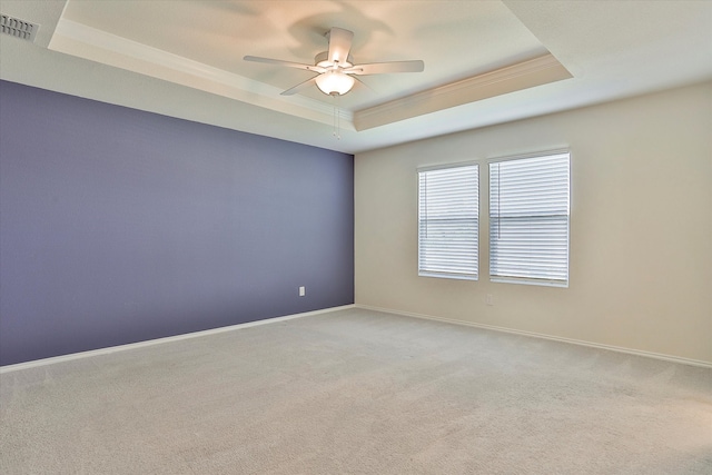 empty room with ceiling fan, light colored carpet, and a raised ceiling