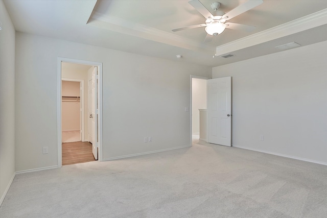 unfurnished bedroom with a spacious closet, light carpet, a tray ceiling, and ceiling fan