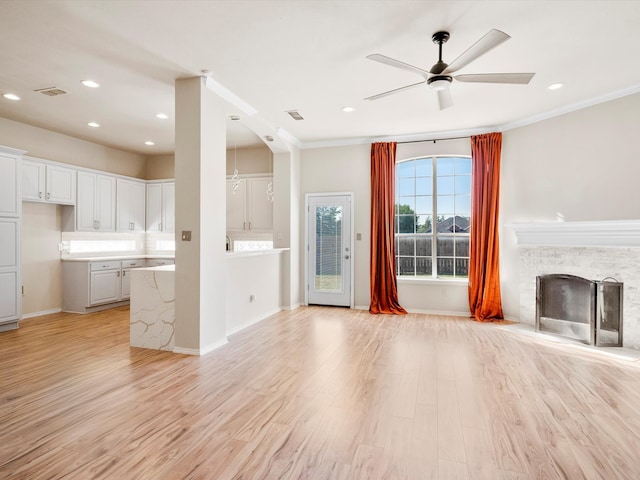 unfurnished living room featuring light hardwood / wood-style floors, a stone fireplace, ceiling fan, and crown molding