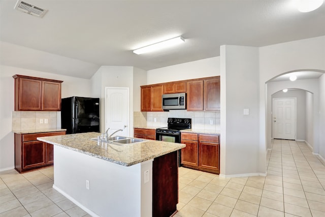 kitchen with tasteful backsplash, light stone countertops, black appliances, sink, and an island with sink