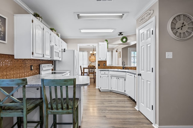 kitchen with white appliances, a kitchen bar, kitchen peninsula, white cabinetry, and crown molding