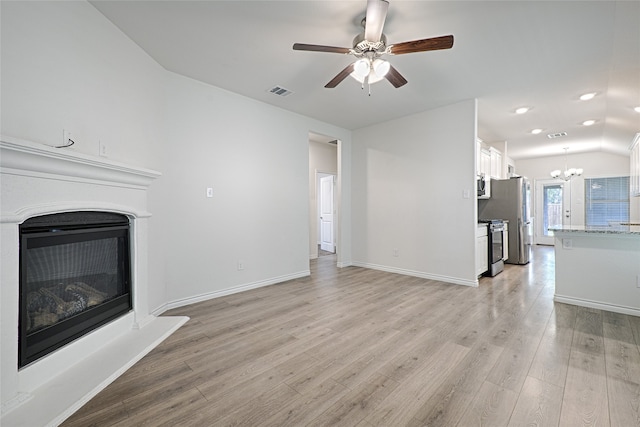 unfurnished living room with vaulted ceiling, ceiling fan with notable chandelier, and light hardwood / wood-style floors