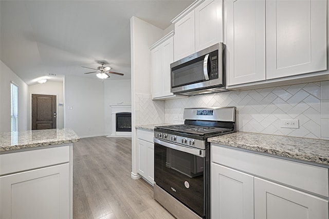 kitchen featuring decorative backsplash, white cabinets, light stone counters, light hardwood / wood-style floors, and stainless steel appliances