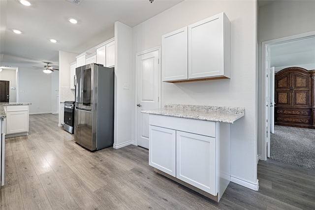 kitchen with white cabinets, ceiling fan, appliances with stainless steel finishes, light wood-type flooring, and light stone counters