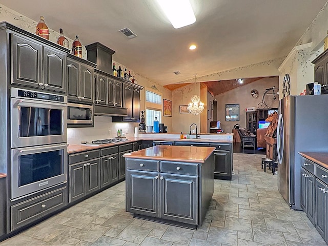 kitchen with kitchen peninsula, sink, vaulted ceiling, decorative light fixtures, and appliances with stainless steel finishes