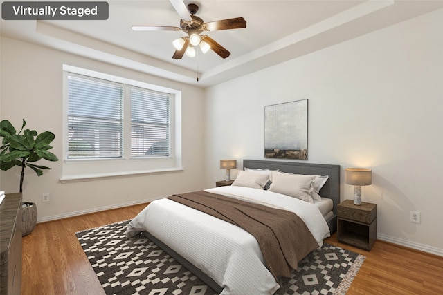 bedroom featuring a tray ceiling, light wood-type flooring, and ceiling fan