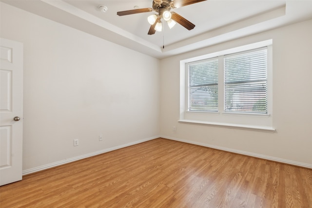 empty room with light hardwood / wood-style flooring, ceiling fan, and a raised ceiling