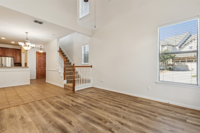 unfurnished living room featuring a notable chandelier, a high ceiling, and light wood-type flooring