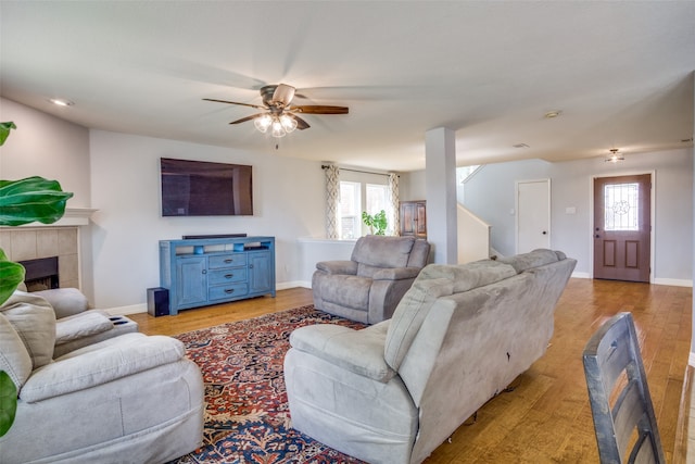 living room with a tiled fireplace, ceiling fan, a healthy amount of sunlight, and light hardwood / wood-style flooring