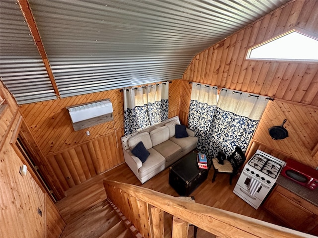 living room featuring lofted ceiling with skylight, wood walls, an AC wall unit, and hardwood / wood-style floors