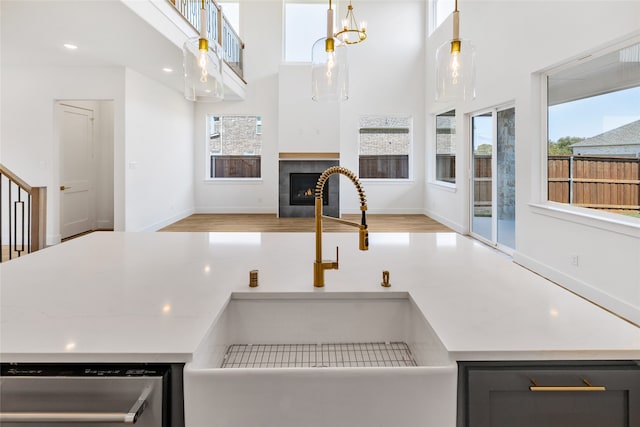 kitchen with a tiled fireplace, dishwasher, pendant lighting, light hardwood / wood-style floors, and sink