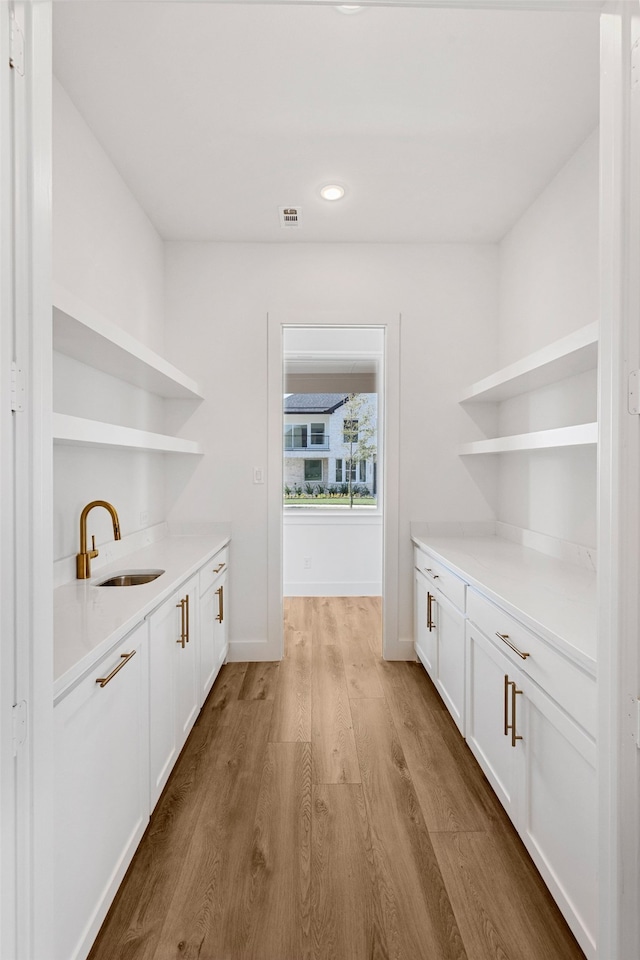 bar with light hardwood / wood-style floors, white cabinets, and sink